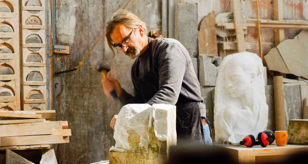 istock Stonemason chiselling a block of stone in workshop 1329520173