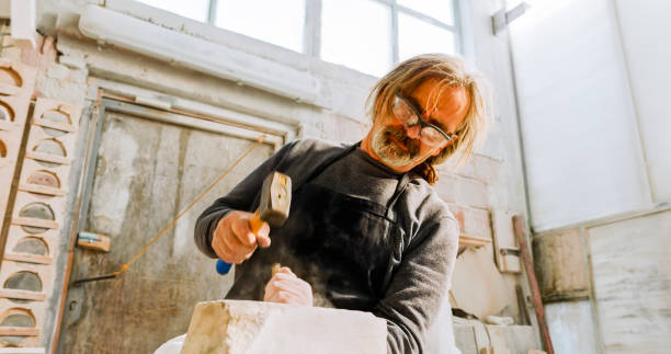 istock Stonemason chiselling a block of stone in workshop 1329520254