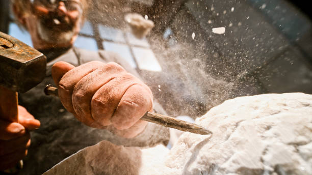 Stonemason chiselling surface of white stone Close-up of stonemason's hands chiselling surface of a white stone sculpture in the workshop. chisel stock pictures, royalty-free photos & images