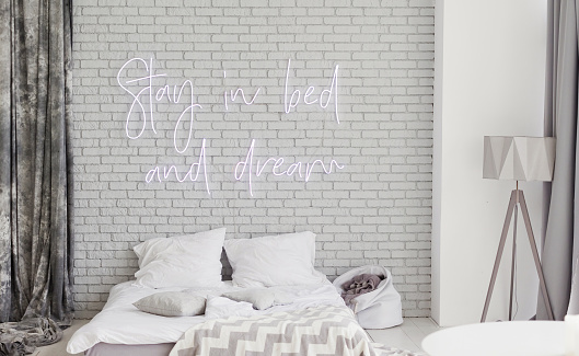 Light loft bedroom with neon sign stay in bed and dream on a grey brick wall