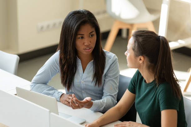 stagisti multietnici ragazze che discutono e completano il compito di formazione sul posto di lavoro - modello di comportamento foto e immagini stock