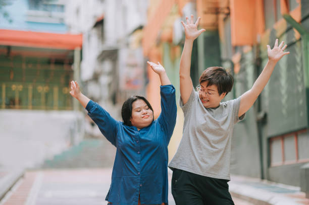 happy asian malay autism down syndrome female  enjoy dancing with her female friend in city street happy asian malay autism down syndrome female  enjoy dancing with her female friend in city street developmental disability stock pictures, royalty-free photos & images