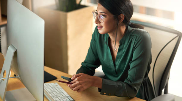 istock Shot of a businesswoman using her smartphone while looking at her PC screen 1329527415