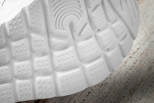 Macro photography of the soles of white sneakers. Children's sports sneakers lying on their side with a white rubber non-slip sole on a wooden background.