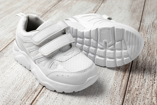 White children's sneakers on a light background. A pair of fashionable sports sneakers with a velcro closure made of leather and fabric and a non-slip sole.