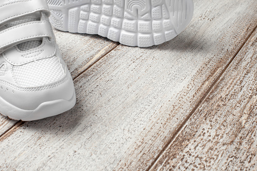 White sneakers on a light background with a place to copy text or design. A pair of fashionable children's leather sneakers sewn with fabric with a non-slip sole and a shoe lying on the side.