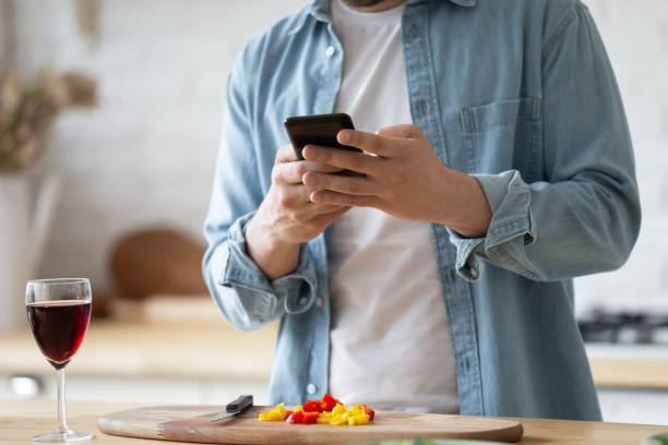 istock Closeup man standing in kitchen holding smart phone chatting online 1329531263