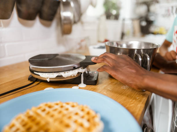 Close-up of waffle iron in kitchen, cooking homemade waffles. Woman preparing yummy breakfast for family