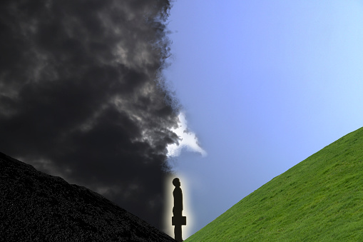 Symmetrical image of a business man with a brief case standing in the valley looking towards the light after coming out of the dark.