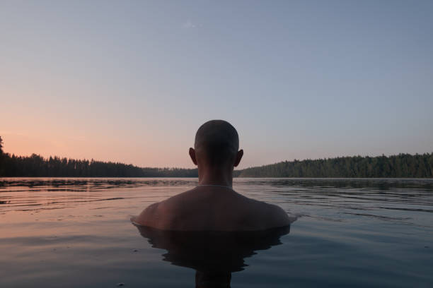 A man swims in a forest lake in the evening. Back view. Alone with nature.