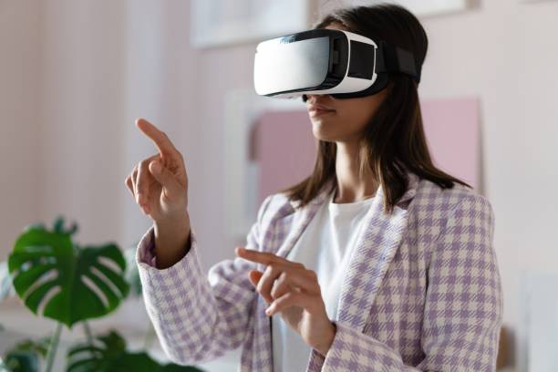 istock Confident young woman in virtual reality headset pointing in the air while standing at her working place in office 1329537177