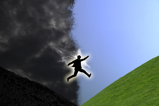 A man jumping towards the light hill coming out of the dark.