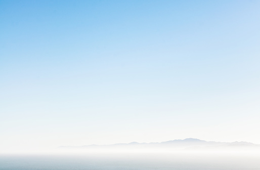 Distant mountains on the horizon over a hazy sea, with a pure blue sky above.