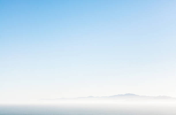 Hazy mountain horizon Distant mountains on the horizon over a hazy sea, with a pure blue sky above. light blue sky stock pictures, royalty-free photos & images
