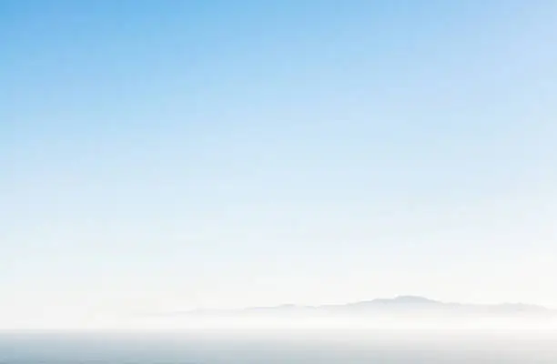 Distant mountains on the horizon over a hazy sea, with a pure blue sky above.