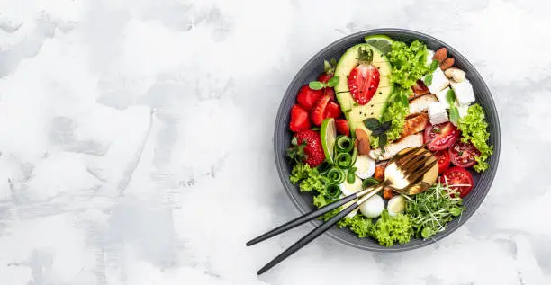 Photo of Grilled chicken, avocado, feta cheese, quail eggs, strawberries, nuts and lettuce on white background, top view. Delicious balanced food concept. Long banner format. top view