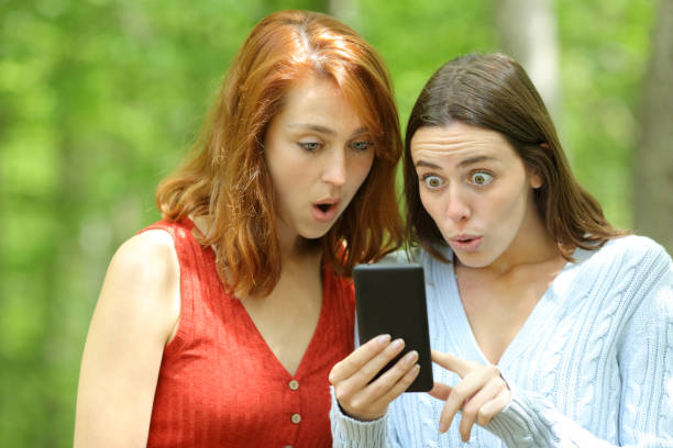 istock Amazed women checking surprising phone content in a park 1329543150