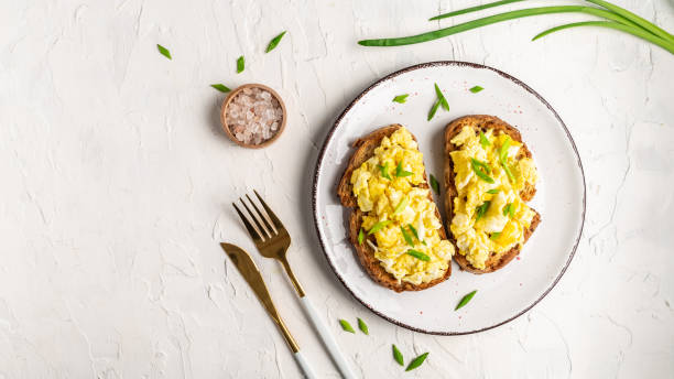 istock Scrambled eggs with green onion on wheat rye wholemeal crispy bread, homemade, healthy breakfast or brunch. Homemade meal, banner, menu recipe place for text, top view 1329543182