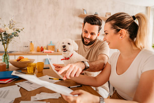 Couple checking their finances at home with their dog Young heterosexual couple sitting in their living room and checking their finances.  Man holding cute toy dog in his lap. refund stock pictures, royalty-free photos & images