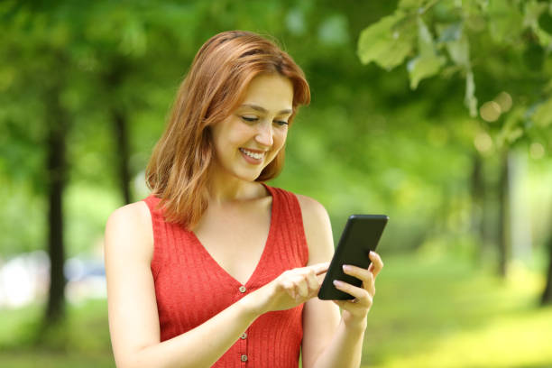 istock Woman in red using mobile phone in a park 1329543988