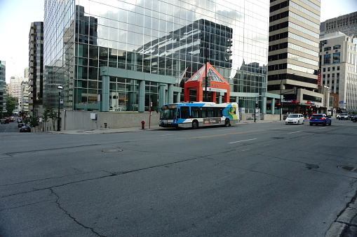 Montreal, QC, Canada - 7-14-2021: stm bus at Sherbrooke street west after the ease of the lockdown of coronavirus and Montreal became in the Green Zone. Background is a business building.
