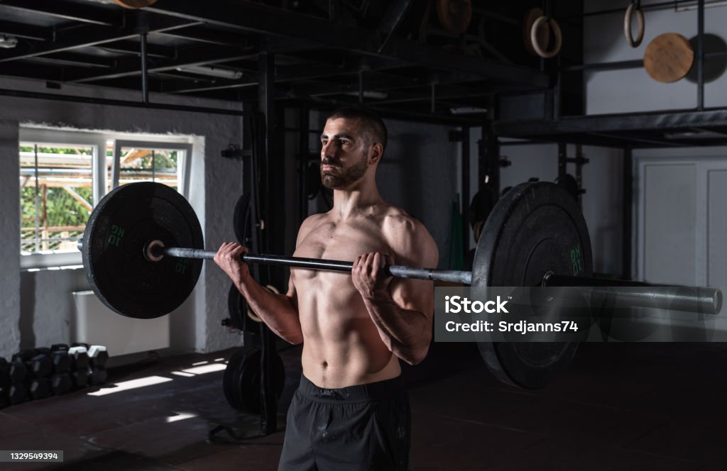 Young active sweaty muscular fit strong man with big muscles doing biceps curly with heavy barbell weight in the gym as hardcore workout cross training real people exercise Bicep Stock Photo