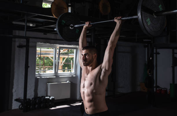 istock Young active strong sweaty fit muscular man with big muscles doing strength shoulder muscles workout in the gym with heavy barbell weights above the head as hardcore cross training 1329549398