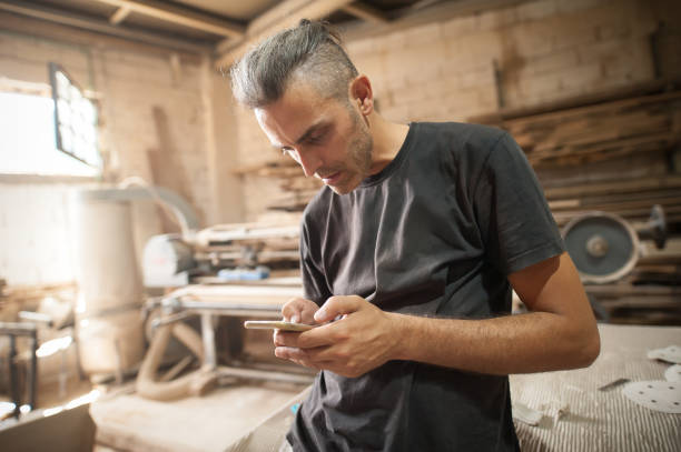 istock Carpenter artisan resting in workshop and scrolling on smartphone 1329549410