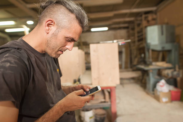 istock Carpenter artisan resting in workshop and scrolling on smartphone 1329549444