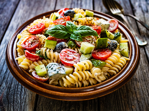 Pasta with fresh vegetables and black olives on wooden table