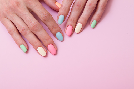 Colored matte gel manicure on female hands on a pink background