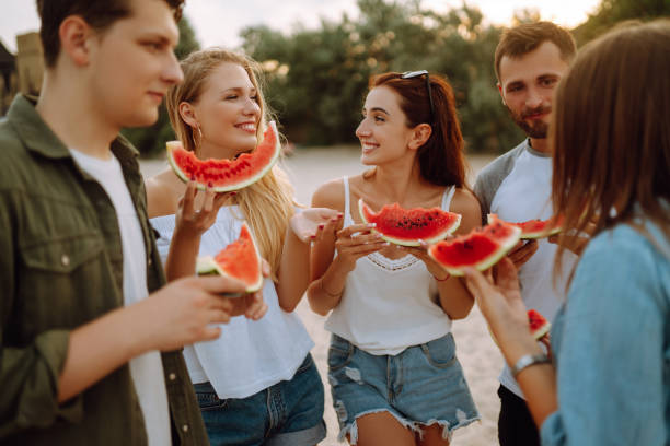 istock Young friends relaxing on the beach and eating watermelon. 1329558847