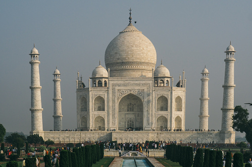 A side view of majestic Tajmahal, one of the world's seven wonders is viewed along with its minaret and lush green garden. A clear blue sky adds magnificence to the white marble of the beautiful architectural structure.