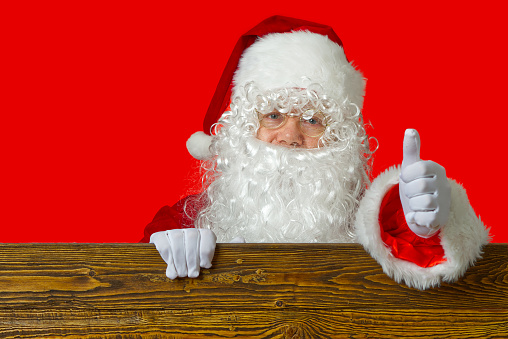 portrait of a cheerful santa claus peeking out from behind a brown wooden shield, copy space