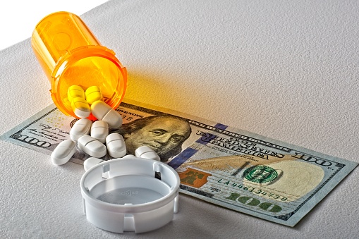 Pharmaceutical cost concept low-angle view of  pill bottle and pills scattered across 100 dollar bill. Side lit.White background.