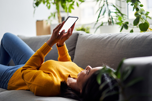 Woman lying on sofa using smartphone with empty screen