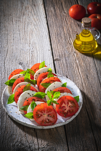 Caprese salad with tomatoes and mozzarella cheese, oregano and olive oil on rustic wooden table board, Mediterranean diet