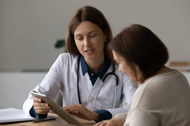 médico serio y amigable hablando con un paciente maduro de la tercera edad, usando gadget - prescription plan fotografías e imágenes de stock