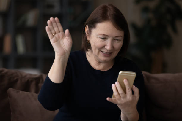 istock Positive senior lady waving hello at smartphone webcam 1329570025