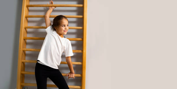 süßes kleines mädchen an sesschnwand, gymnastik- oder sportunterrichtskonzept, kopierraum rechts - kletterwand turngerät stock-fotos und bilder