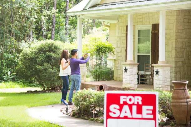 Mid adult couple are considering purchasing a new home.  For sale sign in foreground. stock photo
