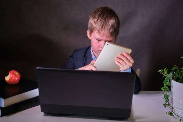 istock A happy boy in a school suit with a digital tablet in his hands, copy space on a dark studio background 1329584824