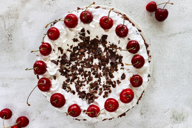 Stock photo showing an elevated view of a homemade, luxury, Black Forest gateau displayed against a marble effect background. imagen de gateau de la selva negra con rosetas de crema batida con tuberías cubiertas con cerezas morello, pastel de chocolate de lujo esmerilado con crema batida y cubierto con virutas de chocolate, fondo de efecto mármol, vista elevada