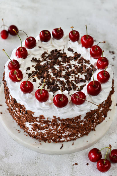 istock Image of Black Forest gateau on cake stand, piped whipped cream rosettes topped with morello cherries, luxury chocolate cake frosted with whipped cream and covered with chocolate shavings, marble effect background, elevated view 1329585710