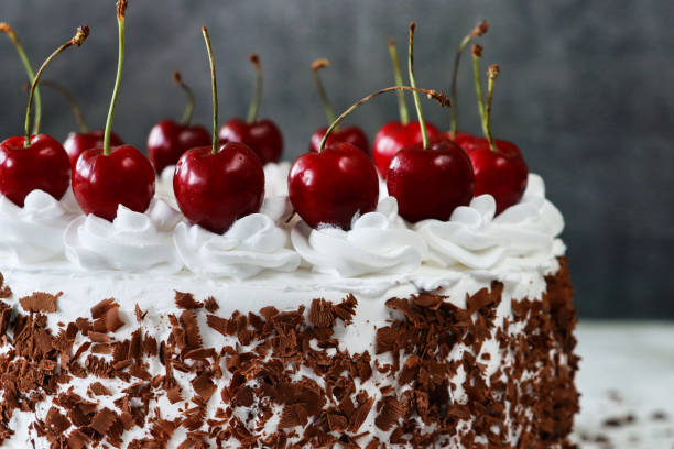 istock Close-up image of Black Forest gateau, piped whipped cream rosettes topped with morello cherries, luxury chocolate cake frosted with whipped cream and covered with chocolate shavings, grey background, focus on foreground 1329586332