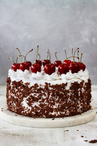 istock Image of Black Forest gateau on cake stand, piped whipped cream rosettes topped with morello cherries, luxury chocolate cake frosted with whipped cream and covered with chocolate shavings, marble effect background, focus on foreground 1329586338
