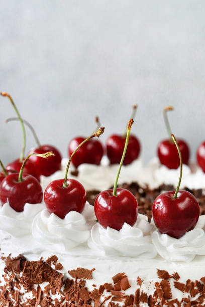 istock Close-up image of piped whipped cream rosettes topped with morello cherries on a Black Forest gateau, luxury chocolate cake frosted with whipped cream and covered with chocolate shavings, marble effect background, focus on foreground 1329586465