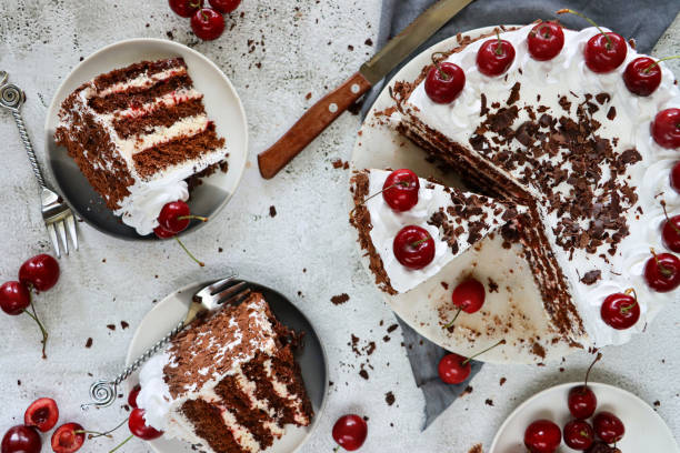 istock Image of Black Forest gateau on cake stand, piped whipped cream rosettes topped with morello cherries, luxury chocolate cake frosted with whipped cream and covered with chocolate shavings, grey muslin, knife, marble effect background, elevated view 1329587545