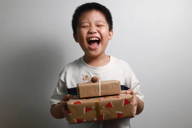 Happy boy receiving Christmas gifts Portrait of a happy Asian boy holding a stack of Christmas gifts against a grey wall. christmas excitement stock pictures, royalty-free photos & images