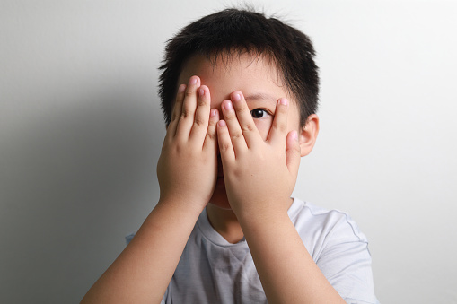 Boy Covering Face With Hands Against White Background